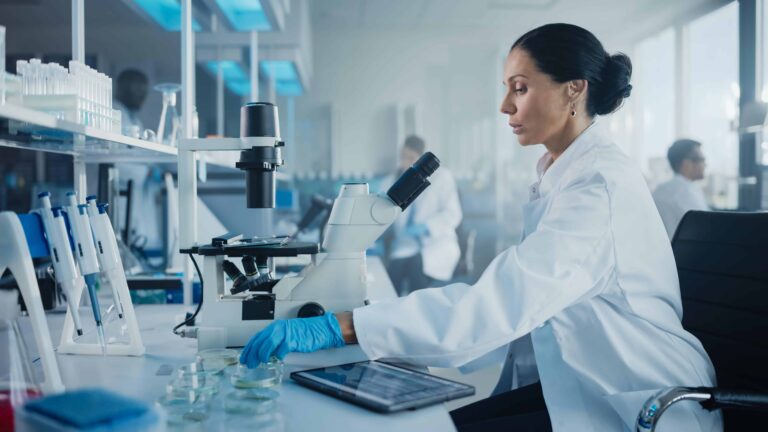 woman lab coat is looking through microscope min